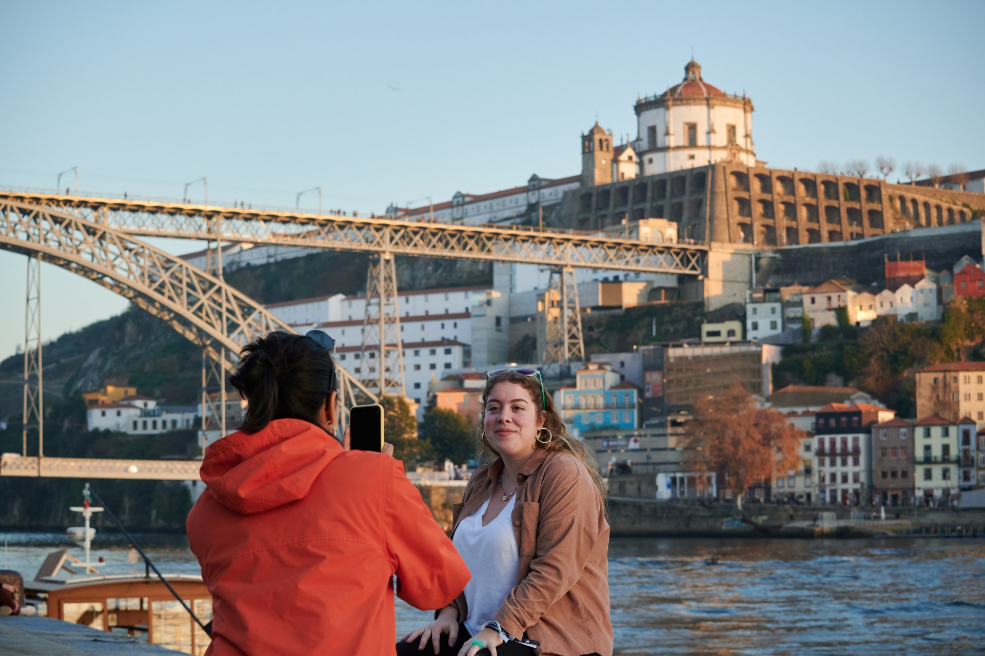 Uma jovem a fotografar a amiga com uma ponte do Porto em fundo
