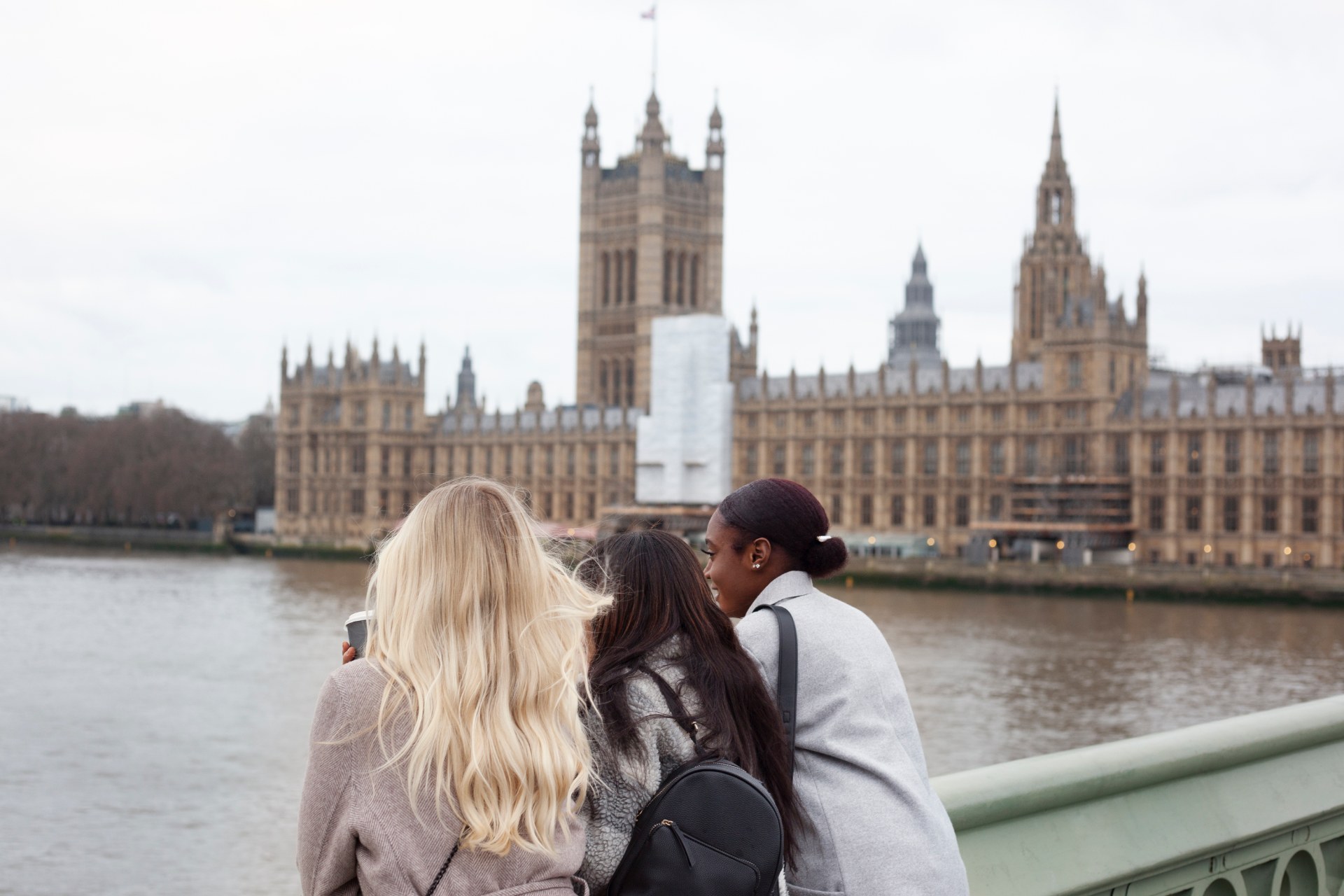 Três jovens junto ao Tamisa, em Londres, com o Palácio de Westminster ao fundo